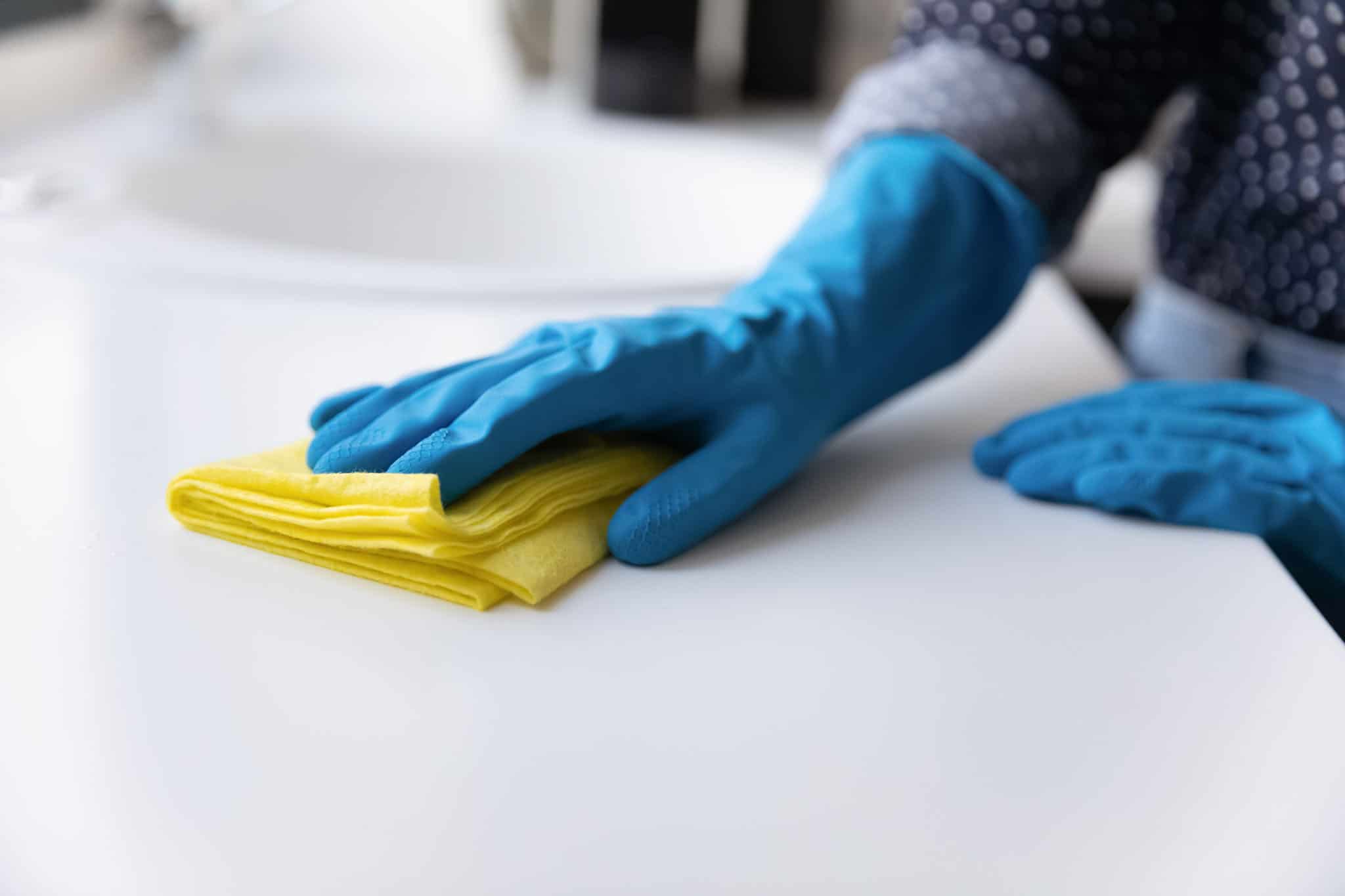 Crop close up of woman in rubber gloves clean counters in kitchen. Female housekeeper or housewife do daily home cleaning routine use napkin wipe dust and mud from table or desk. Housekeeping concept.